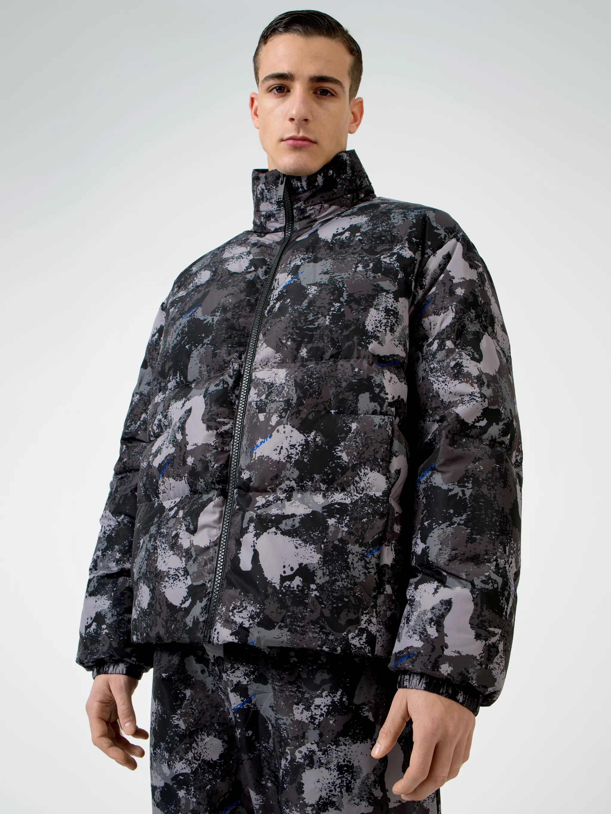 Tonal grey/royal blue camouflage print padded jacket from Marcelo Burlon County of Milan featuring camouflage print, stand-up collar, front zip fastening, two side patch pockets, long sleeves, elasticated cuffs and straight hem.