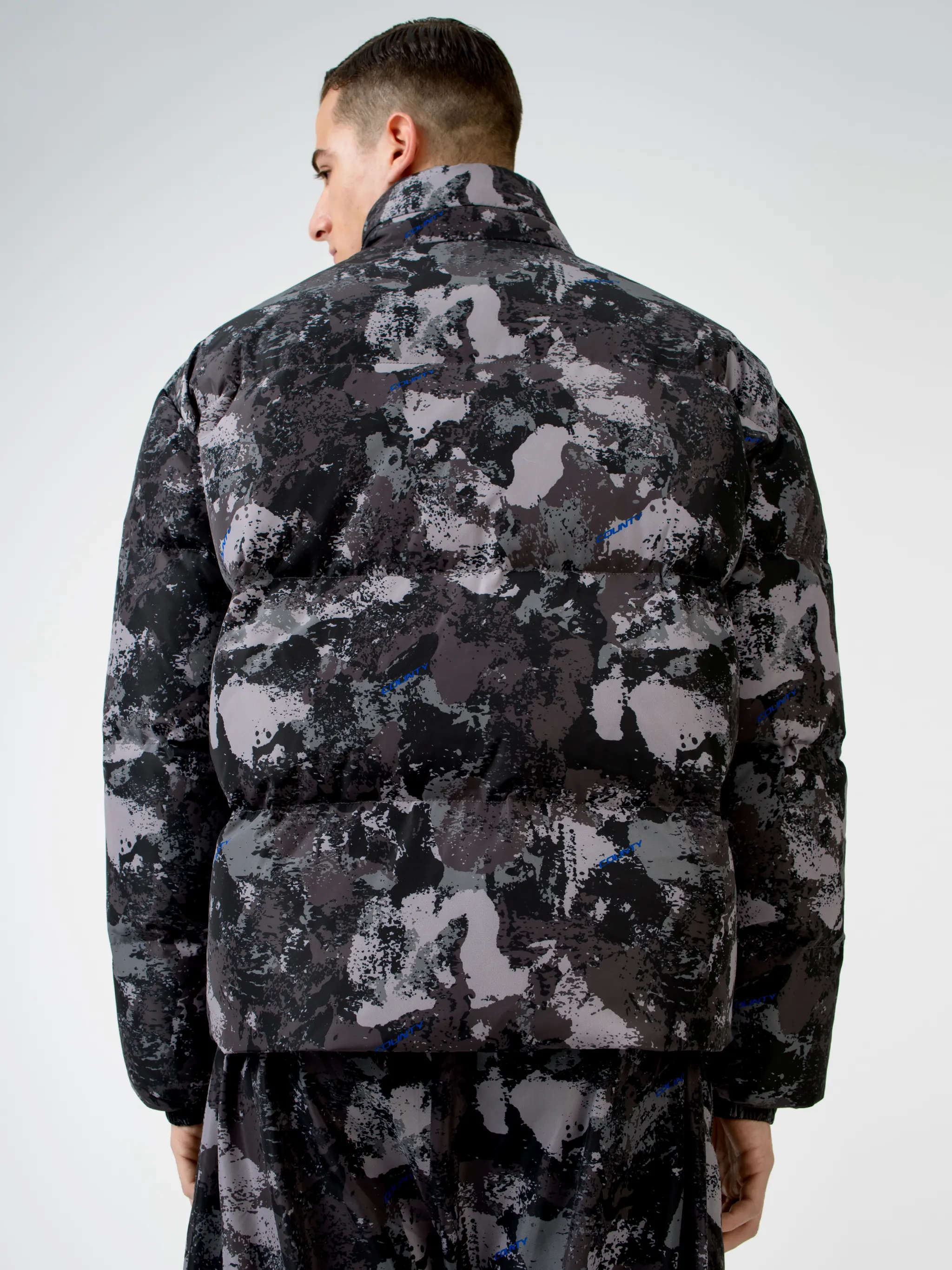 Tonal grey/royal blue camouflage print padded jacket from Marcelo Burlon County of Milan featuring camouflage print, stand-up collar, front zip fastening, two side patch pockets, long sleeves, elasticated cuffs and straight hem.