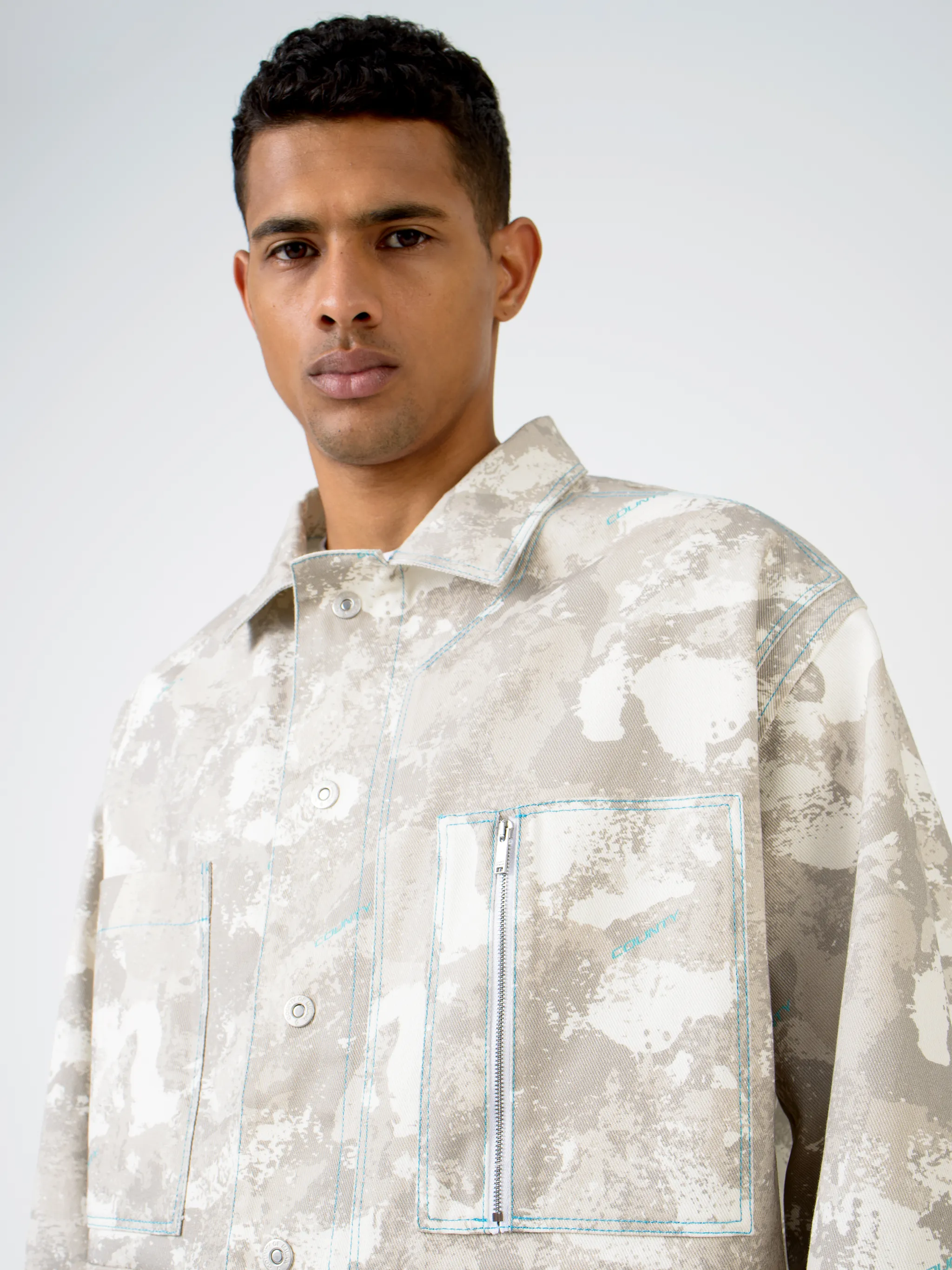 Tonal-beige cotton camouflage print military jacket from Marcelo Burlon County of Milan featuring camouflage print, classic collar, front button fastening, chest patch pocket, zip-fastening chest pocket, two side button-fastening pockets, long sleeves, buttoned cuffs and straight hem.
