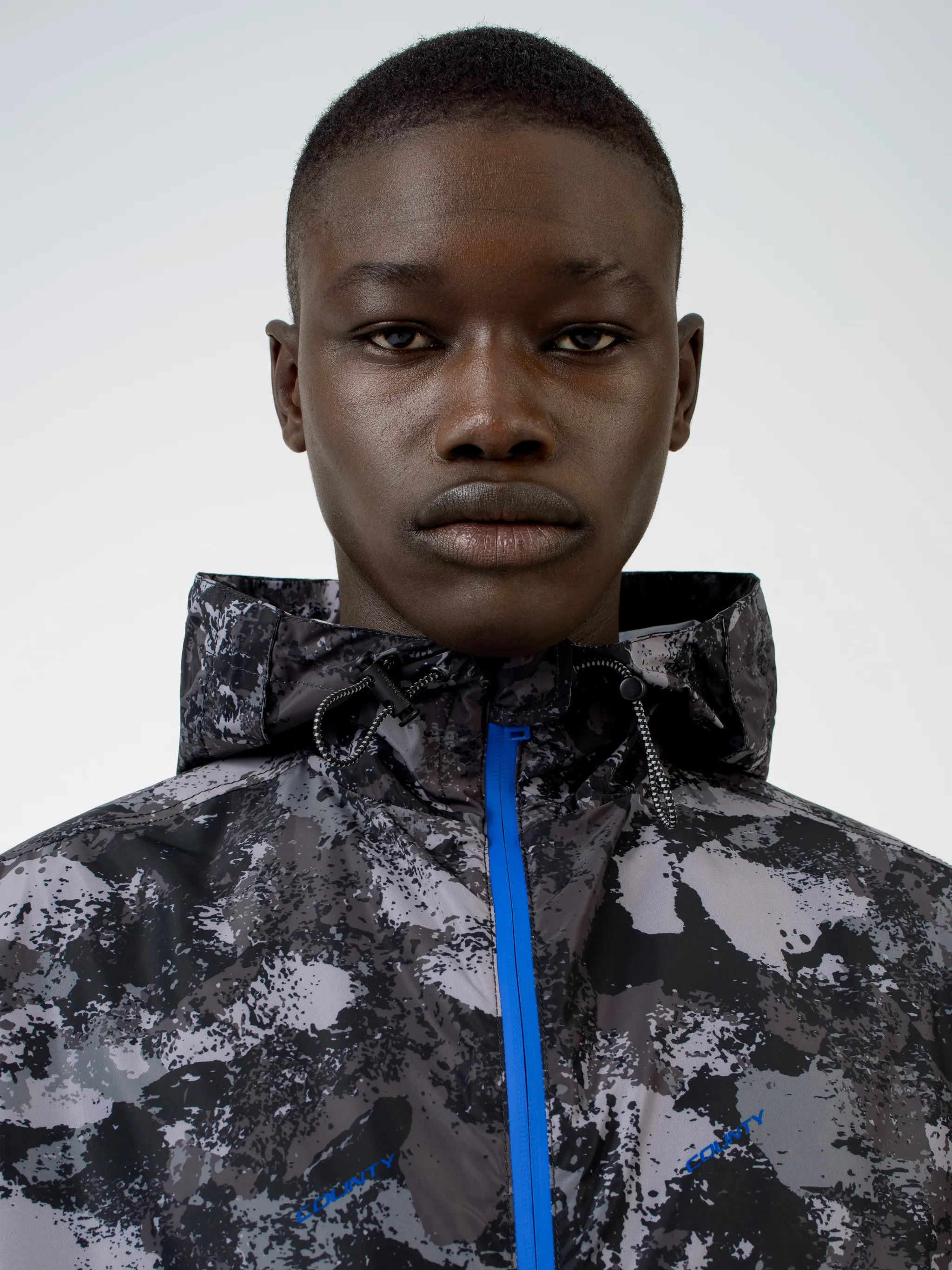 Tonal grey/royal blue camouflage print hooded windbreaker from Marcelo Burlon County of Milan featuring camouflage print, drawstring hood, front zip fastening, two side patch pockets, long sleeves and drawstring hem.