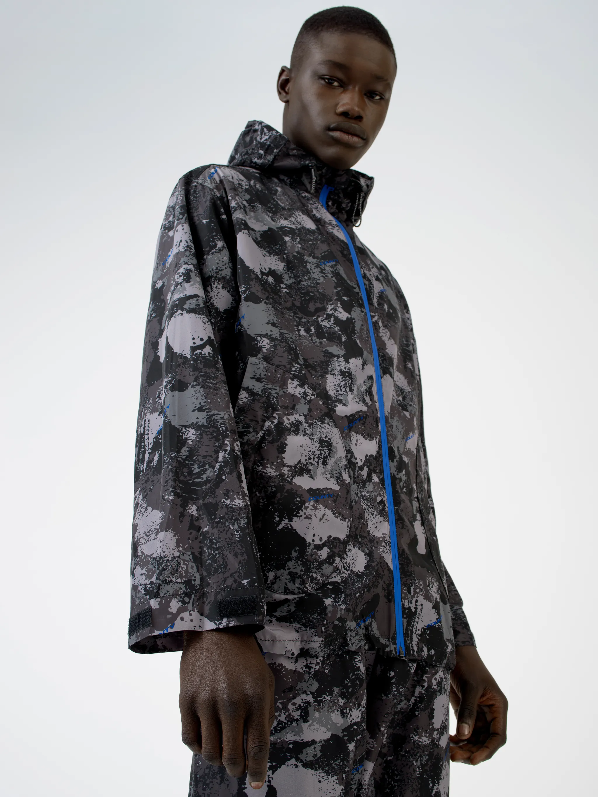 Tonal grey/royal blue camouflage print hooded windbreaker from Marcelo Burlon County of Milan featuring camouflage print, drawstring hood, front zip fastening, two side patch pockets, long sleeves and drawstring hem.