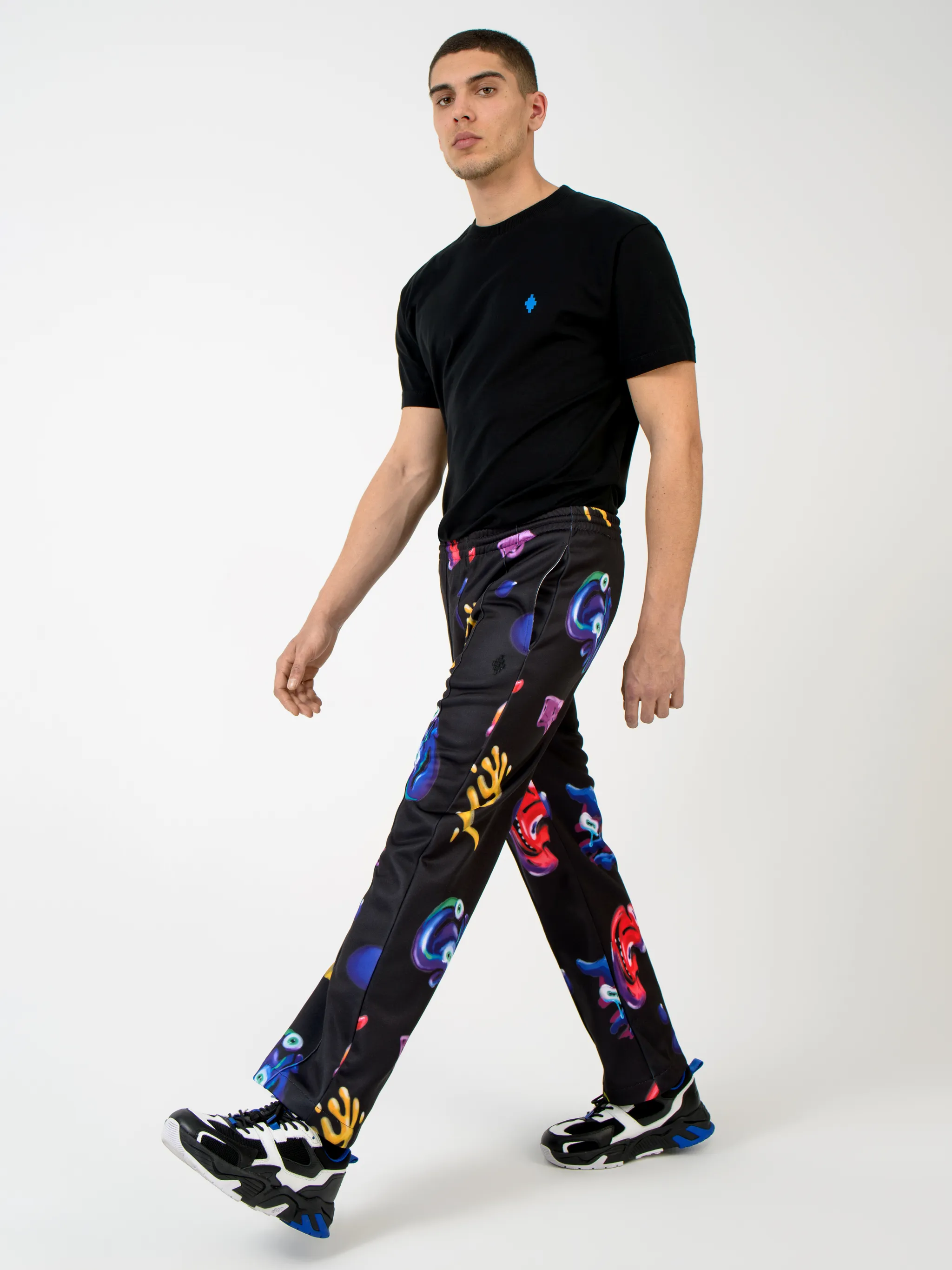 Black/multicolour cotton-blend Crazy Faces print track pants from Marcelo Burlon County of Milan featuring graphic print, elasticated waistband, drawstring fastening, piped-trim detailing, two side patch pockets and straight leg.