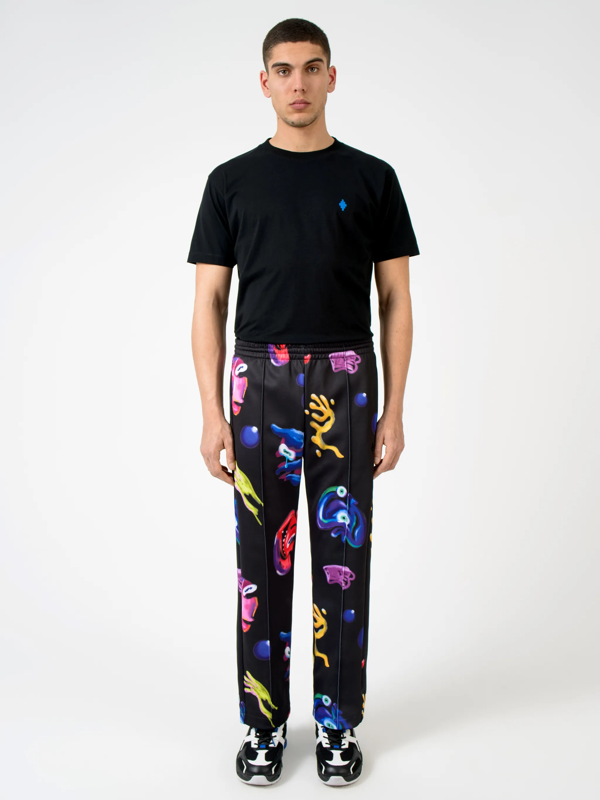 Black/multicolour cotton-blend Crazy Faces print track pants from Marcelo Burlon County of Milan featuring graphic print, elasticated waistband, drawstring fastening, piped-trim detailing, two side patch pockets and straight leg.