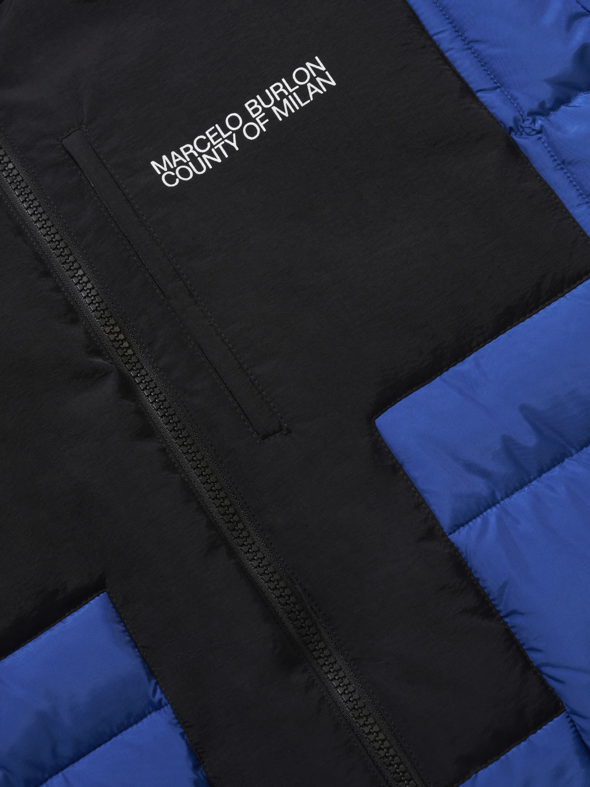 Blue/black recycled nylon-blend quilted cross block jacket from Marcelo Burlon County of Milan featuring signature Cross motif, quilted, two-tone design, logo print at the chest, funnel neck, long sleeves, front zip fastening and two zip-fastening pockets. POSITIVELY CONSCIOUS: This Planet Conscious product is crafted from certified recycled or upcycled materials, which helps you make a better choice for the environment as they generate less energy, save water and reduce the need for new raw materials. For recycled synthetic clothing products we highly recommend using a microfibre-catching washing bag to ensure that no microplastics that can pollute water are released in the process..