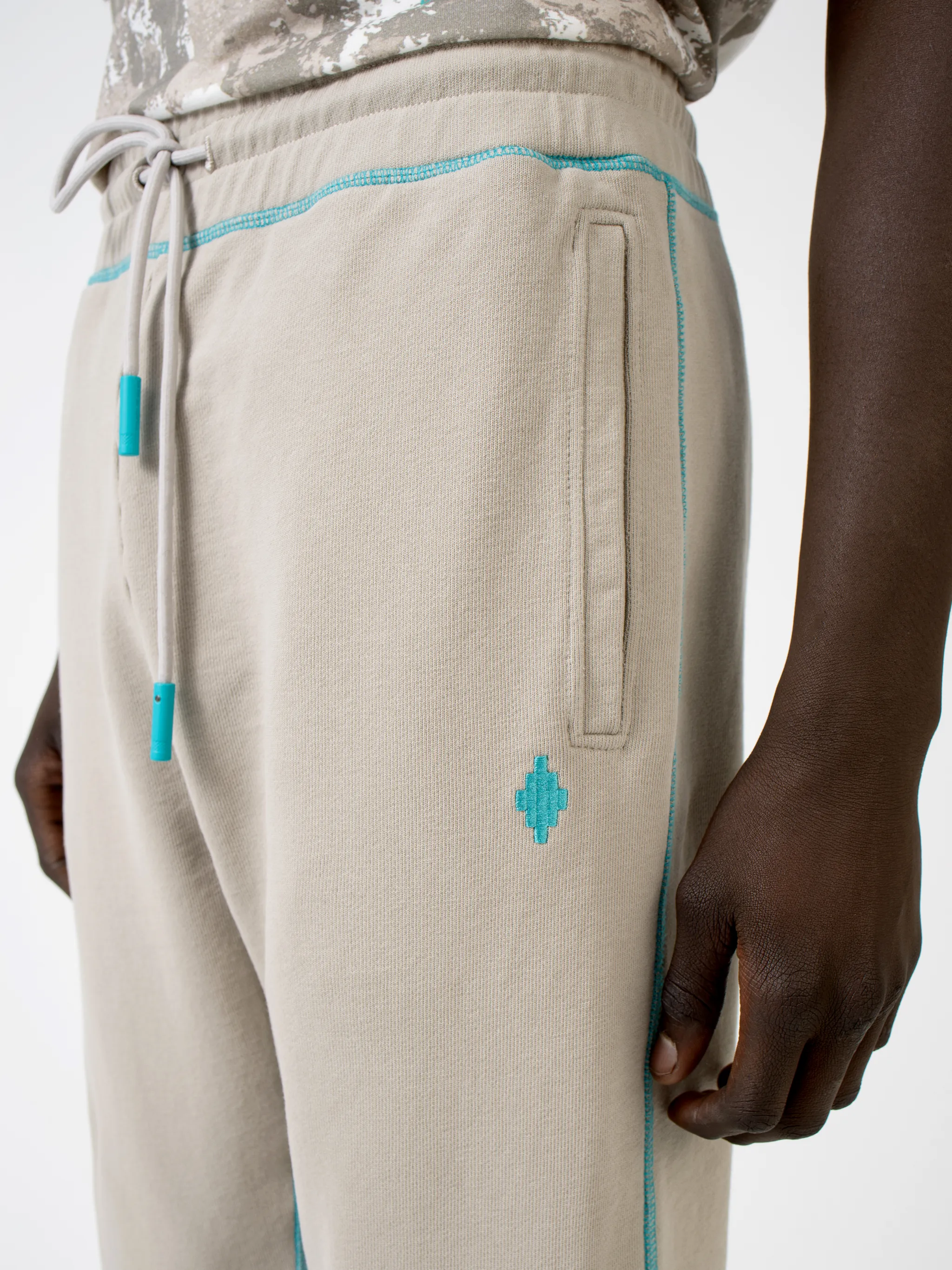Beige cotton Cross tapered track pants from Marcelo Burlon County of Milan featuring embroidered logo to the rear, contrasting trim, elasticated ankles, elasticated waistband, drawstring fastening, tapered design, two side slit pockets and rear welt pocket.