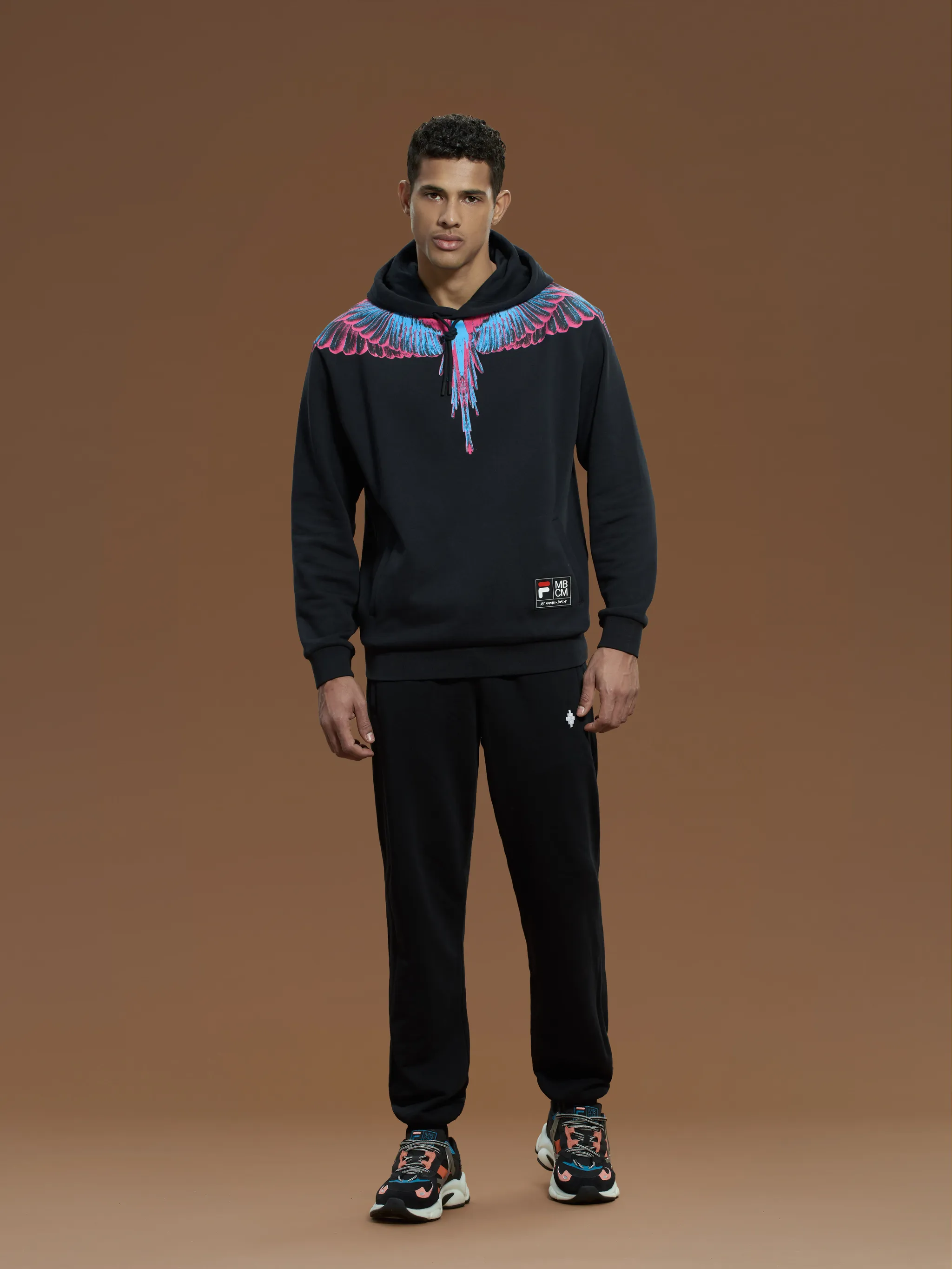 Black/pink/blue cotton x FILA Wings-print drawstring hoodie from Marcelo Burlon County of Milan featuring signature Marcelo Burlon Wings print, logo patch to the front, crew neck, drawstring hood, long sleeves, front pouch pocket and straight hem.