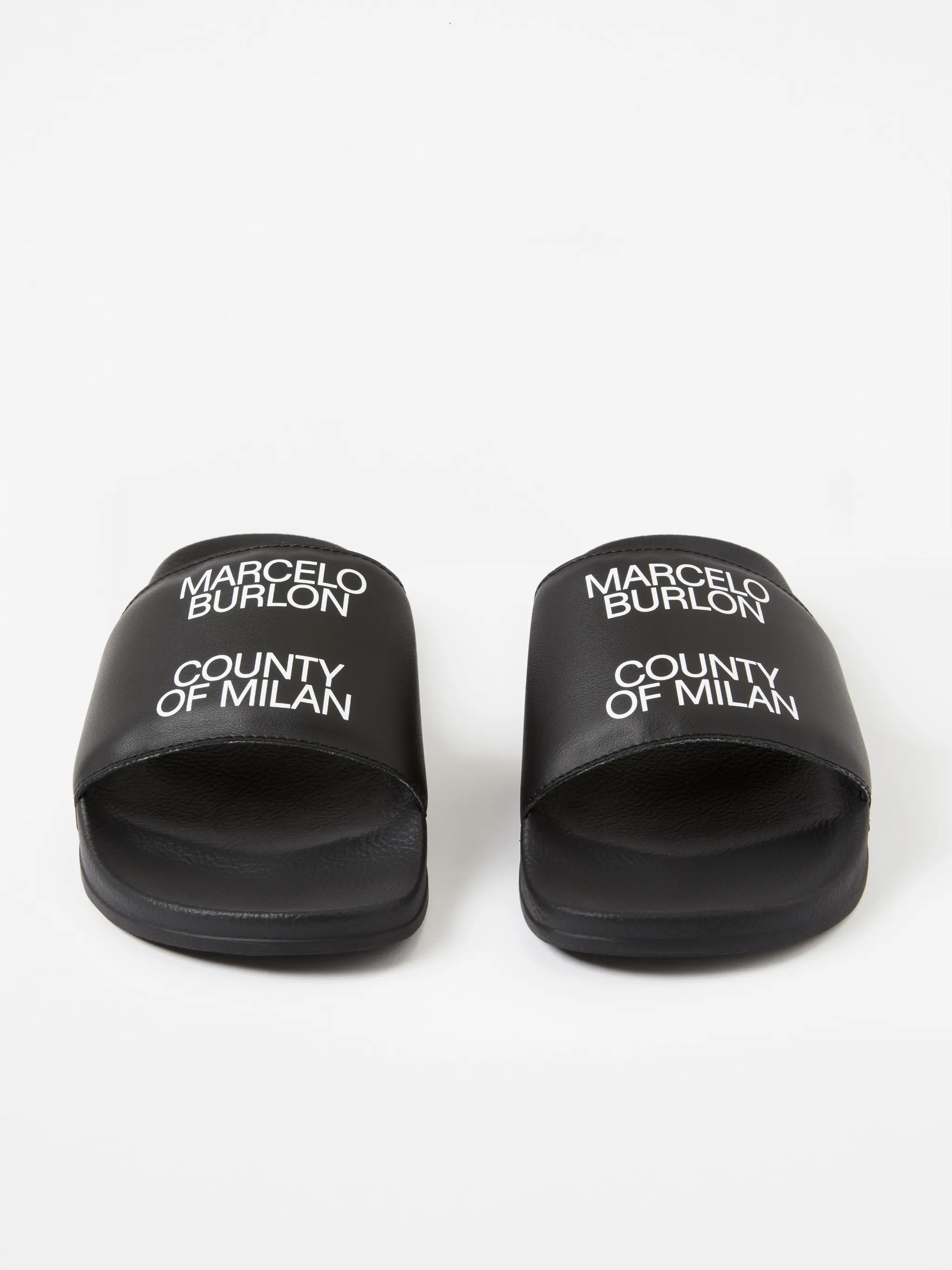 Black/white leather logo sliders from Marcelo Burlon County of Milan featuring slip-on style and all-over logo print.
