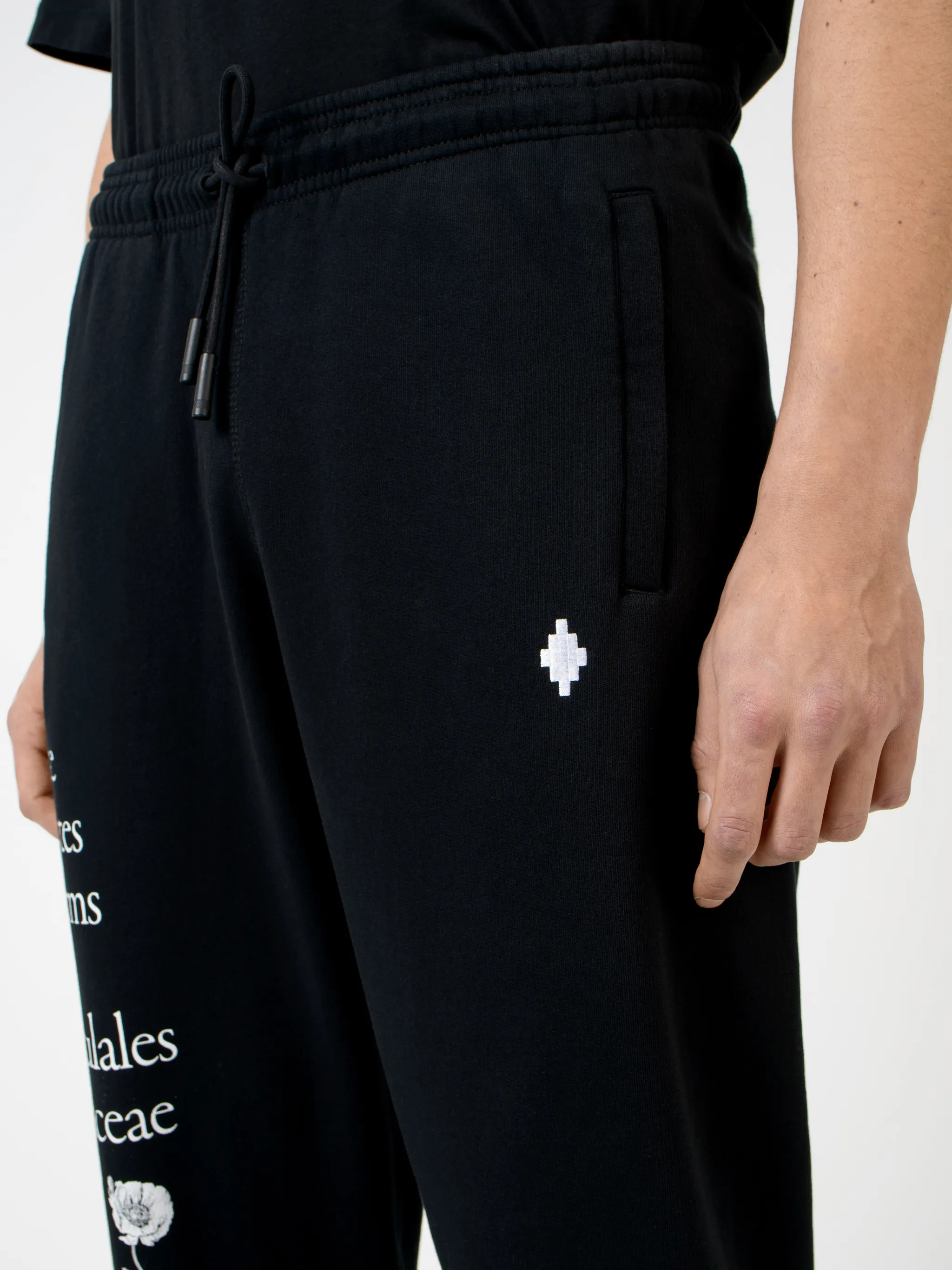 Black cotton Papaver tapered track pants from Marcelo Burlon County of Milan featuring embroidered logo to the front, slogan print, elasticated ankles, elasticated waistband, drawstring fastening, tapered design, two side slit pockets and rear welt pocket.