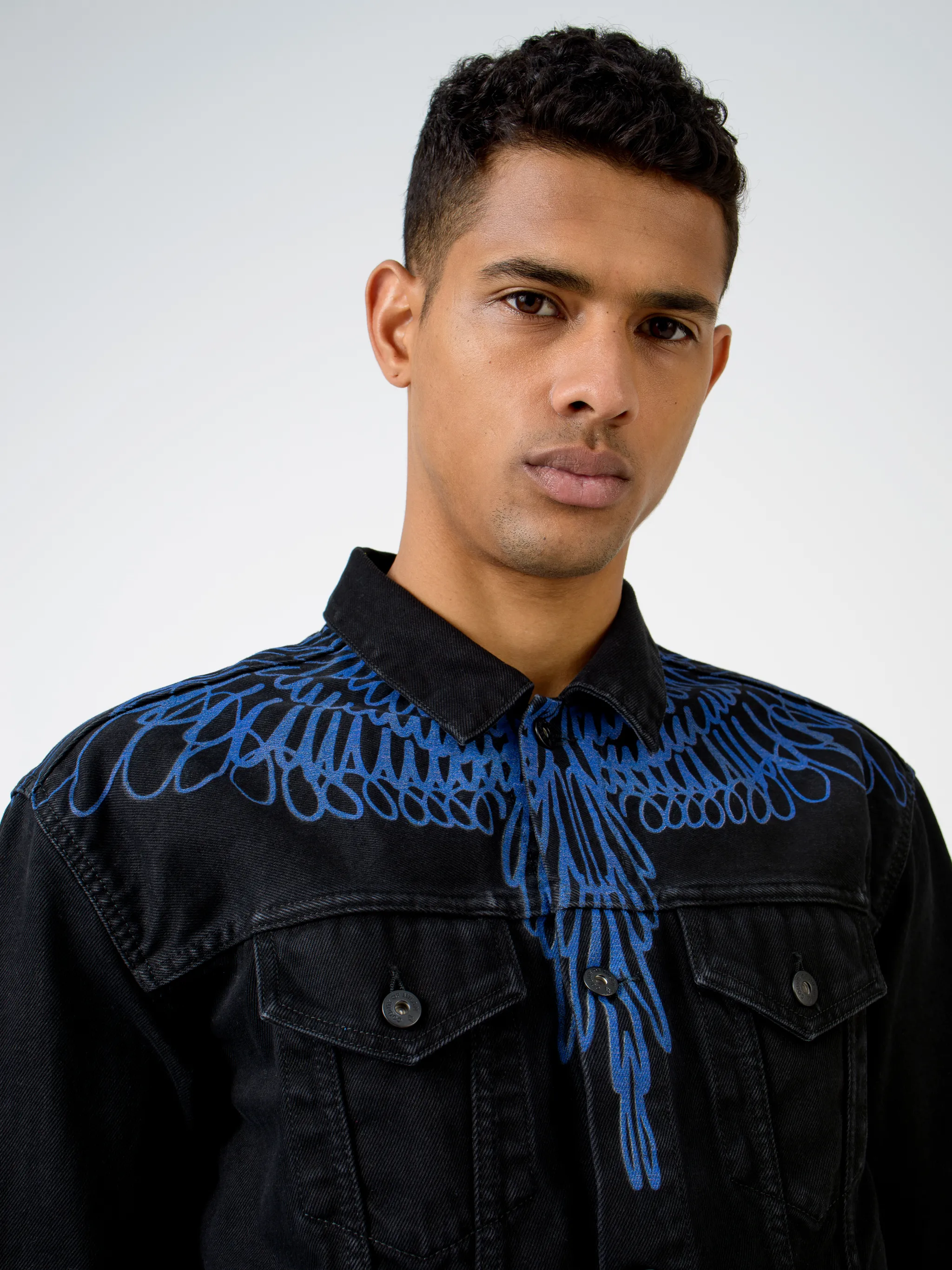 Black/blue cotton Pictorial Wings denim jacket from Marcelo Burlon County of Milan featuring wings print, front button placket, two chest flap pockets, two side slit pockets, long sleeves, buttoned cuffs and logo patch to the rear.