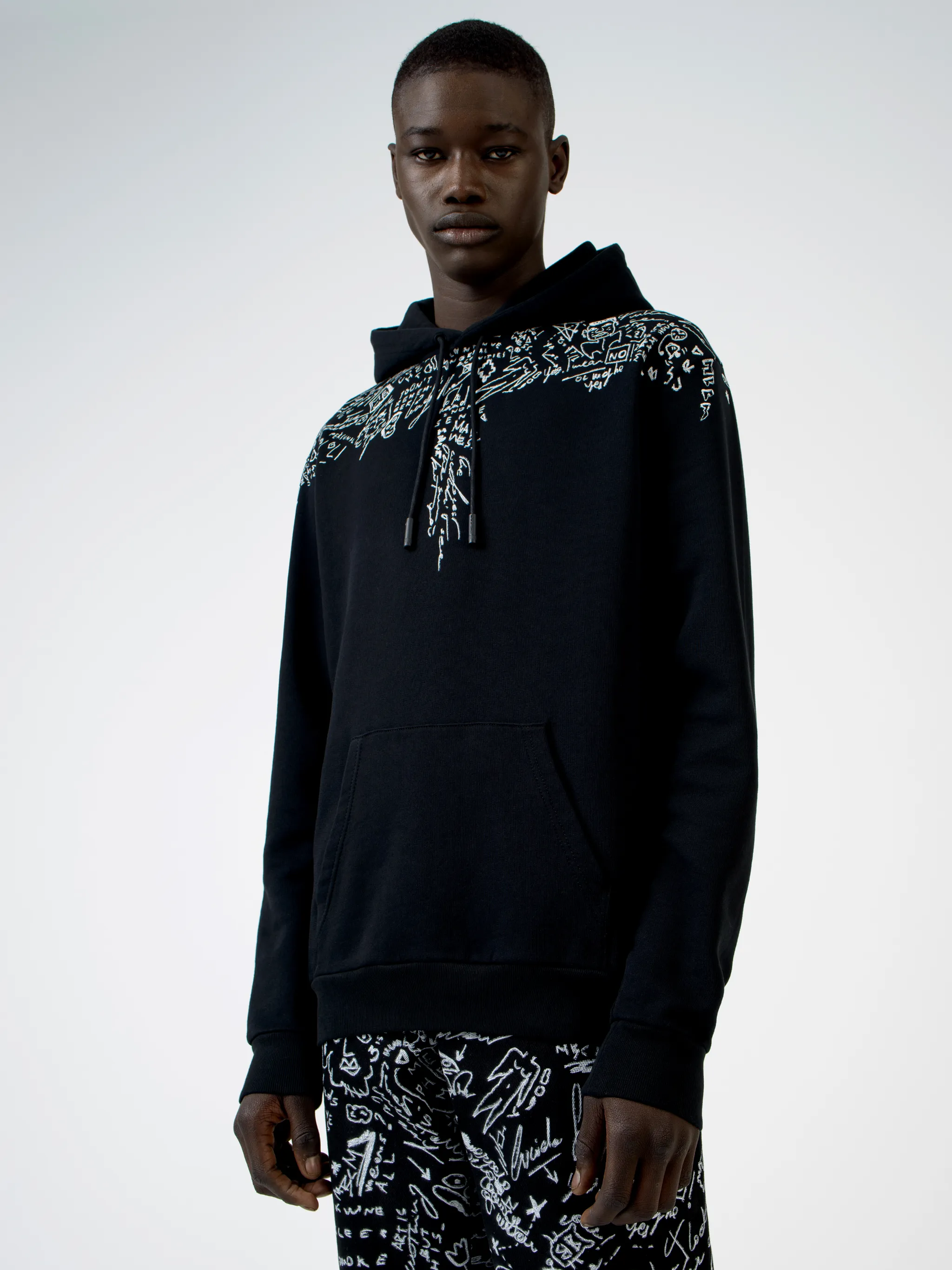 Level up on your casualwear with this black cotton hoodie from Marcelo Burlon County of Milan, printed with doodle logo prints across the chest and shoulders. Get the sketchpad out. Featuring a drawstring hood, a graphic print, long sleeves and a kangaroo pocket.